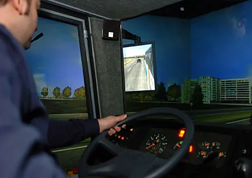 Conductor profesional al volante de un simulador, con la carretera proyectada en las pantallas frontales