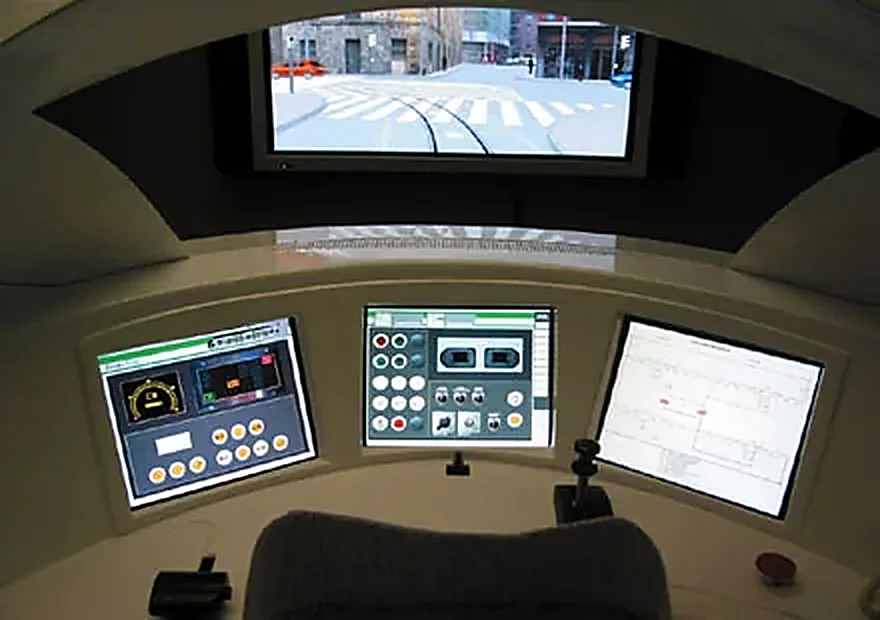 Interior de la cabina del simulador de tranvía: pantalla con la vía urbana, cuadro de mandos y monitores del puesto de conducción